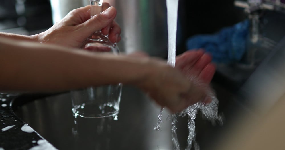 Person holding a hand under running water while waiting for it to warm, illustrating water heater repair issues.